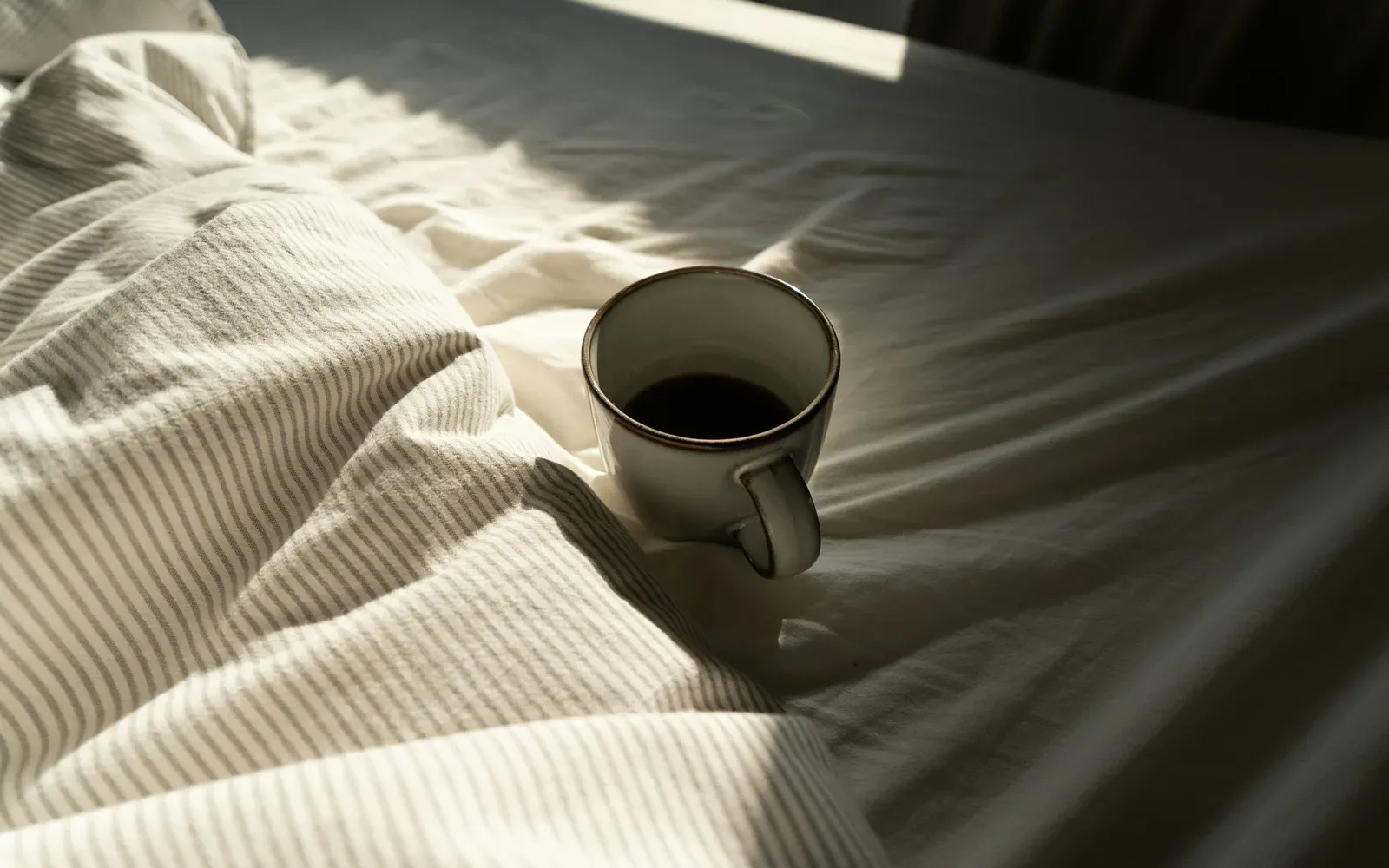 Kaffeetasse auf zerwühlter weißer Bettwäsche im Morgenlicht – Freundschaft Plus mit klaren Regeln