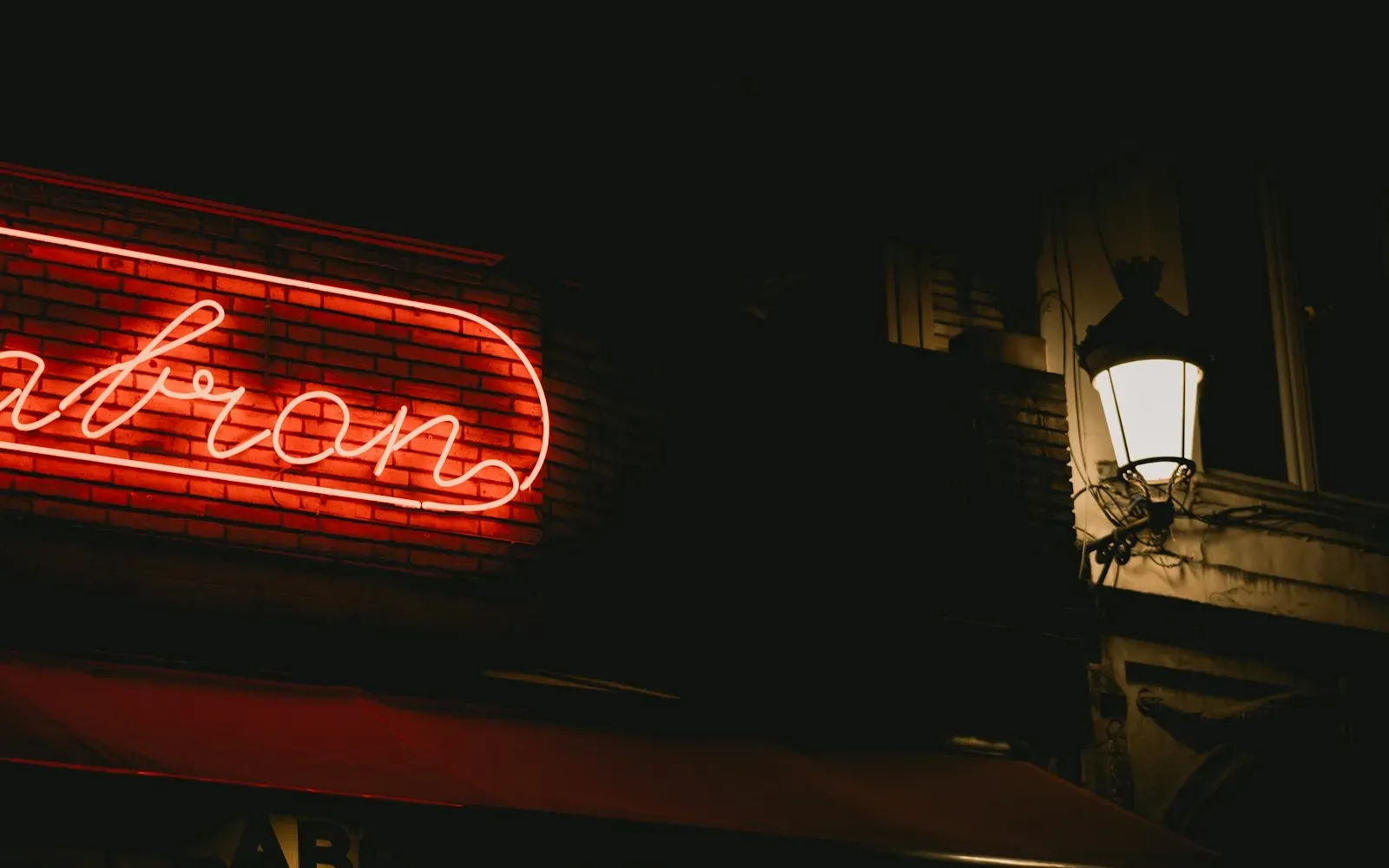 Rot leuchtende Neonschrift an einer Hauswand neben einer Straßenlaterne bei Nacht